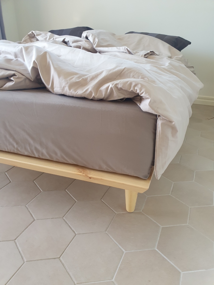 Close-up corner view of the raw pine Air Bed 160x200 cm frame, illustrating the joinery detail of the frame and the profile of one of the angled support legs.