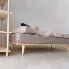 Vue en contre-plongée d’un cadre de lit Air 90 × 200 en pin clair non traité avec literie, placé à côté d’une grande étagère Air assortie, sur un sol carrelé hexagonal.