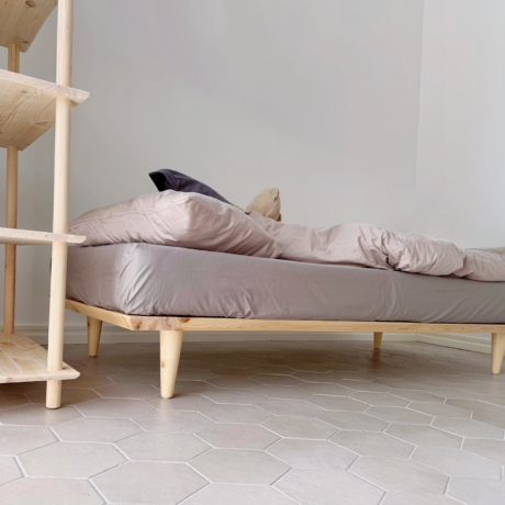 Vue en contre-plongée d’un cadre de lit Air 90 × 200 en pin clair non traité avec literie, placé à côté d’une grande étagère Air assortie, sur un sol carrelé hexagonal.