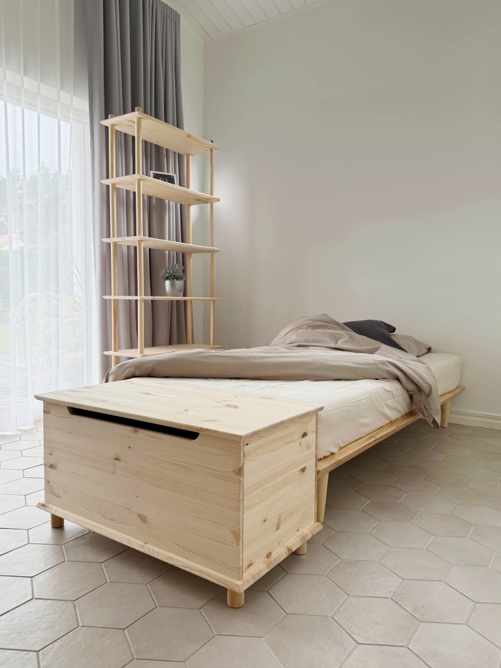 Un coffre Air en pin non traité est placé au pied d’un cadre de lit Air 90 × 200 avec matelas, à côté d’une grande étagère modulaire Air, dans une chambre d’enfant lumineuse.