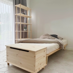 Eine Air Truhe aus unbehandeltem Kiefernholz steht am Fußende eines Air Bettgestells 90x200 mit Matratze, neben einer hohen modularen Air Regal-Einheit in einem lichtdurchfluteten Kinderzimmer.