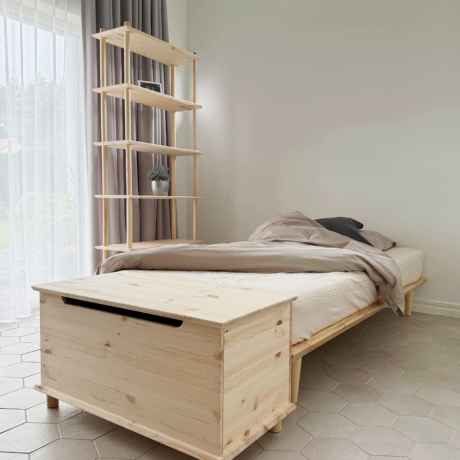 Eine Air Truhe aus unbehandeltem Kiefernholz steht am Fußende eines Air Bettgestells 90x200 mit Matratze, neben einer hohen modularen Air Regal-Einheit in einem lichtdurchfluteten Kinderzimmer.