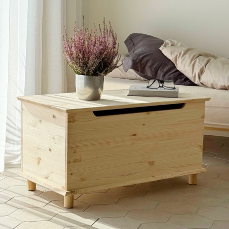 Coffre Air en pin clair non traité, avec une plante en pot et des lunettes posées dessus, placé à côté d’un cadre de lit Air avec une literie neutre, sur un sol carrelé.