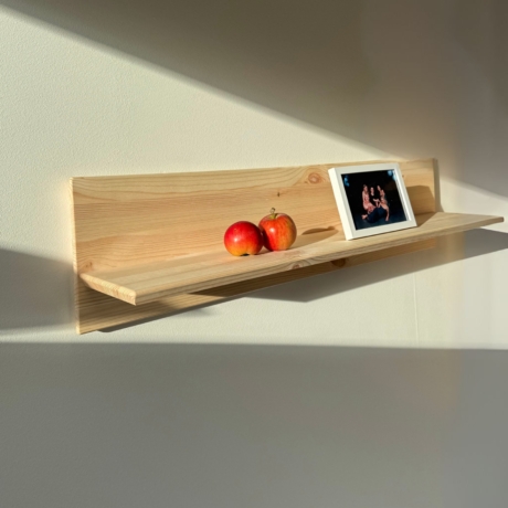 Image lifestyle de l’étagère murale Air ROHE en pin brut, montée sur un mur blanc, présentant un cadre photo et deux pommes, éclairée par la lumière naturelle du soleil.