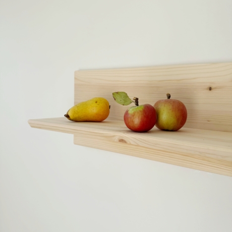 Gros plan de l’étagère murale Air en pin clair non traité, montée sur un mur blanc, présentant une poire jaune et deux pommes rouges et vertes, mettant en valeur les détails du grain du bois.