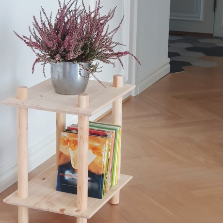 Vue lifestyle de l’étagère modulaire à deux niveaux en pin brut, placée dans un coin de la pièce, mise en scène avec un pot argenté de bruyère violette et une pile de livres colorés sur l’étagère inférieure.