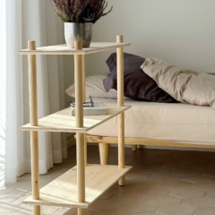 Étagère Air étroite en pin clair non traité, avec une plante en pot et des livres, placée à côté d’un cadre de lit Air avec literie, sur un sol carrelé baigné de lumière naturelle.