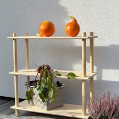 Photo lifestyle en extérieur de l’étagère Air large à trois niveaux en pin brut, mettant en scène deux citrouilles orange sur l’étagère supérieure et un panier de betteraves fraîches sur l’étagère intermédiaire, à côté d’une plante de bruyère en pot.