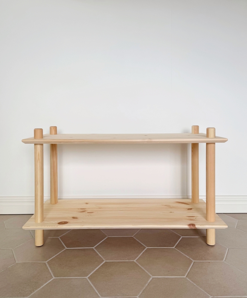 Large étagère modulaire Air à deux niveaux en pin brut, vide, mise en valeur contre un mur blanc et un sol clair à carreaux hexagonaux, soulignant la pureté de son design.