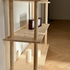 Lifestyleaufnahme des breiten, zweistöckigen modularen Air Regals aus unbehandeltem Kiefernholz, gestaltet mit einer violetten Heidepflanze im Topf auf der oberen Ablage, einer dekorativen Holzuhr und einem Buch auf dem unteren Regal, vor einer weißen Wand.