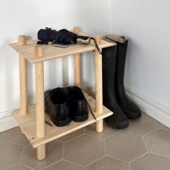 Photo lifestyle de l’étagère modulaire Air à deux niveaux en pin brut, placée dans un coin d’entrée, accueillant des chaussures noires et un parapluie, avec des bottes de pluie posées à côté.
