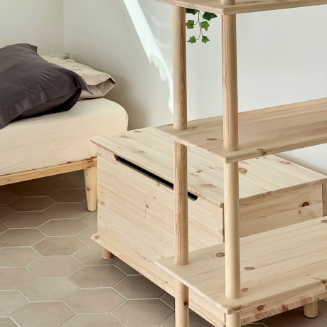 Vue d’ensemble de la pièce mettant en scène la grande étagère Air à six niveaux en pin brut, le coffre de rangement en bois assorti et le cadre de lit Air 90 × 200, illustrant un design de chambre minimaliste et cohérent.