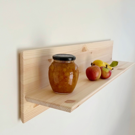 An untreated light pine Air wall shelf mounted on a white wall, displaying a glass jar of jam and two apples and a pear.