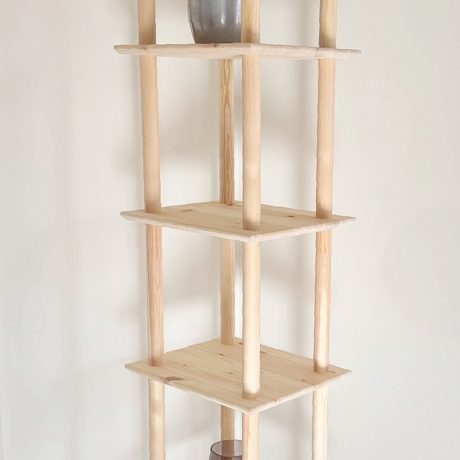 Full-height lifestyle shot of the raw pine Air Shelf narrow six-tiered unit, standing neatly in a room corner, styled with a succulent plant and a brown glass vase.